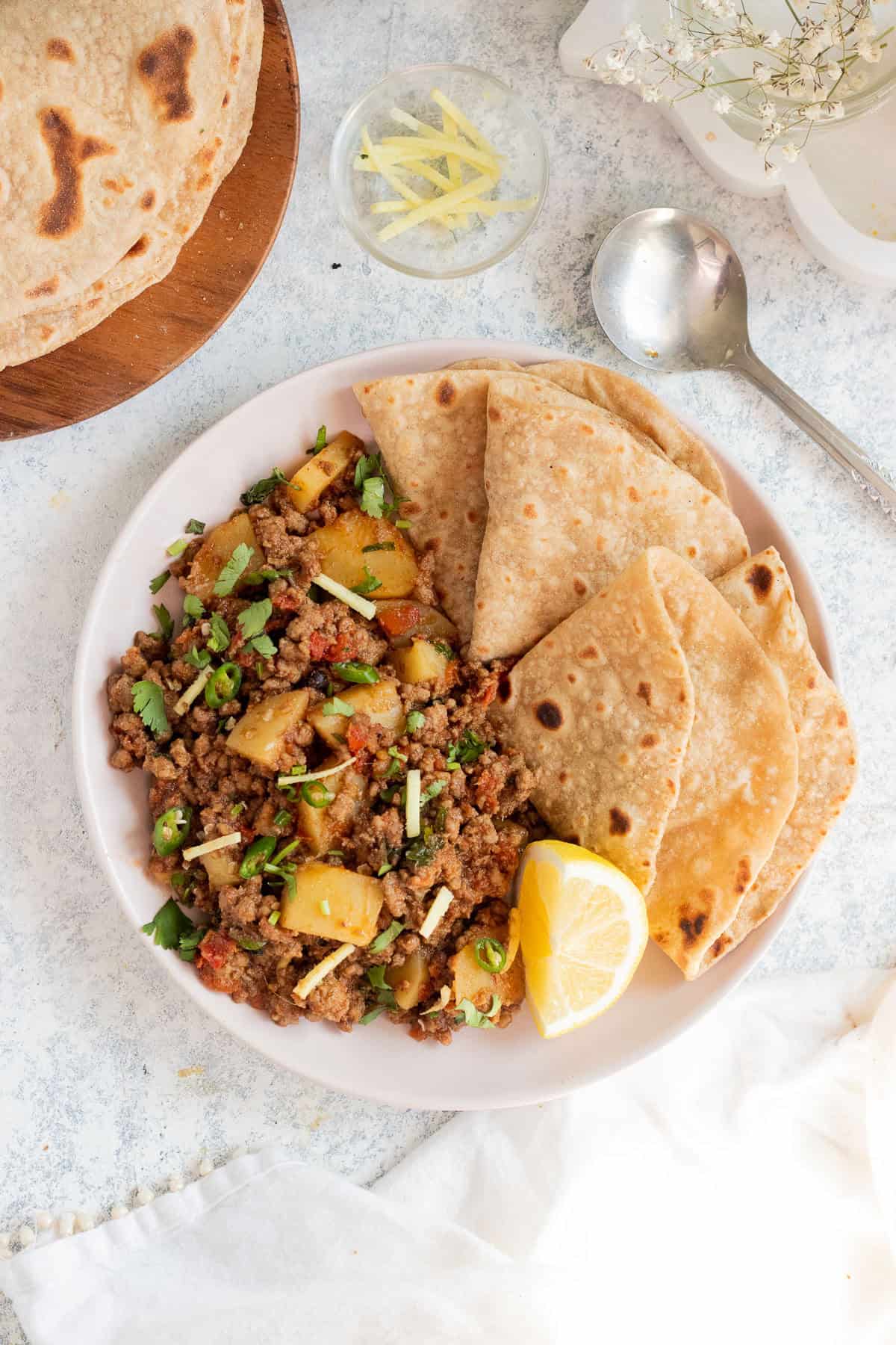 a plate with qeema aloo, roti, and a lemon wedge