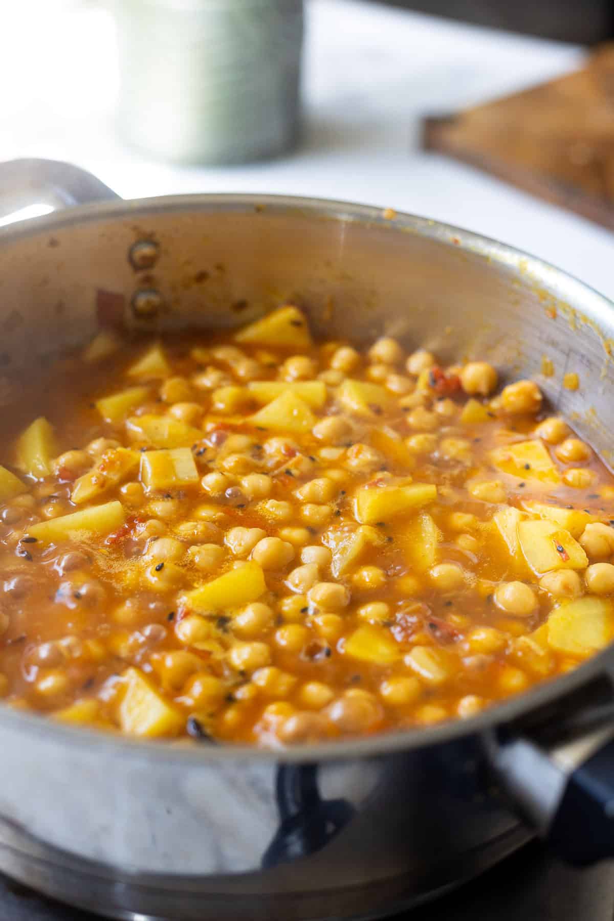 A stainless steel pot filled with a simmering aloo chana stew-chickpeas and diced potatoes in a rich, orange-colored sauce-rests invitingly on the kitchen countertop.