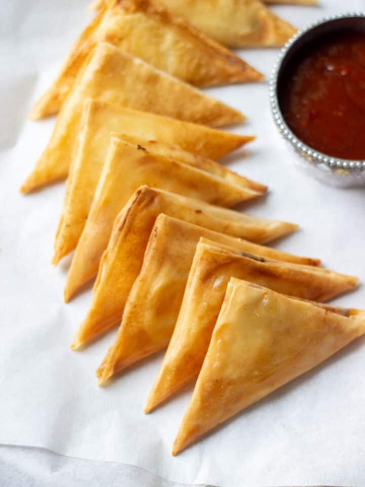 Cheese Samosas in a tray with chili sauce on the side in a bowl