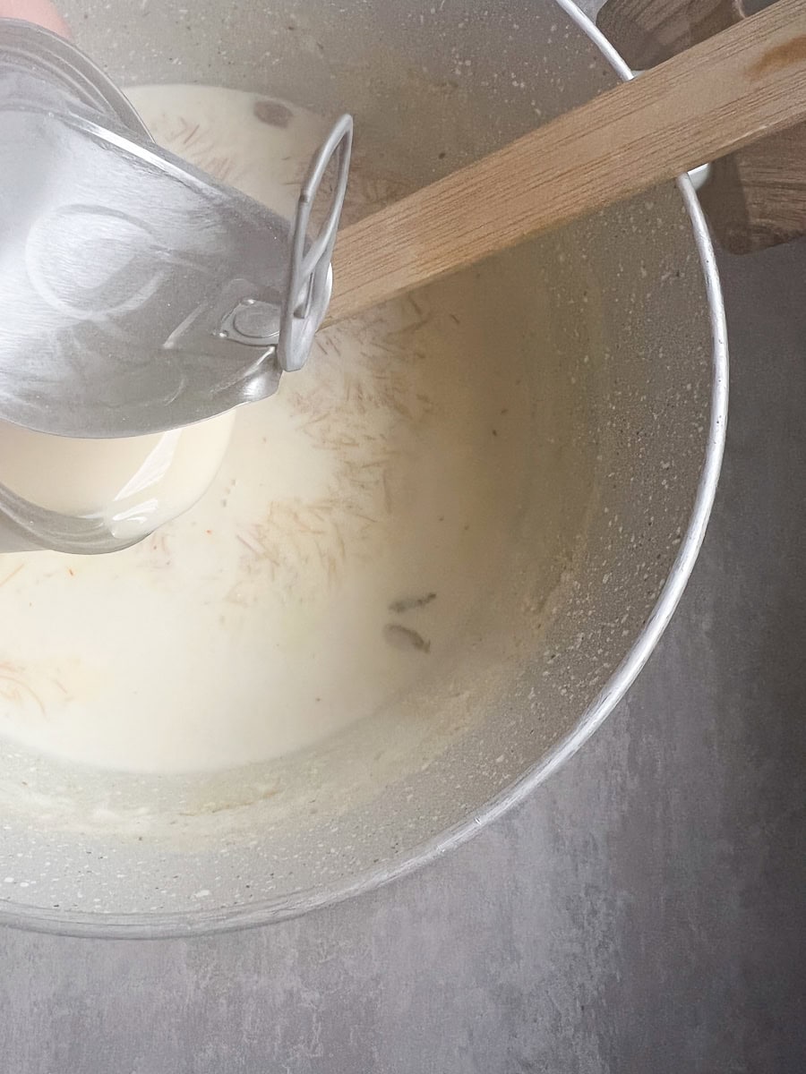 condensed milk being poured into a pot of sheer khurma