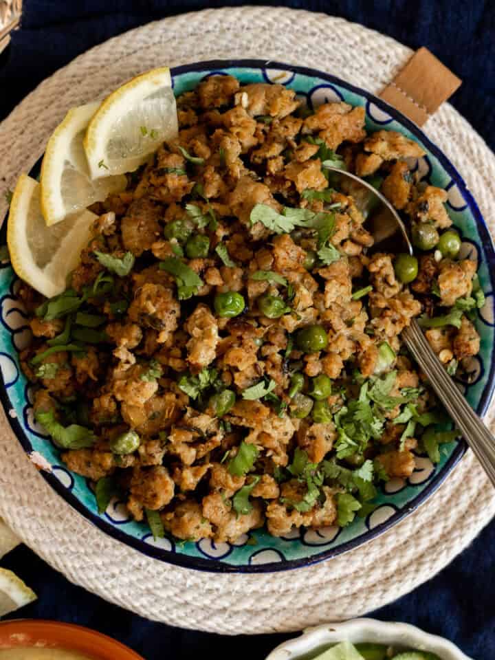 Top down view of a bowl of chicken keema garnished with cilantro and pieces of lemon.
