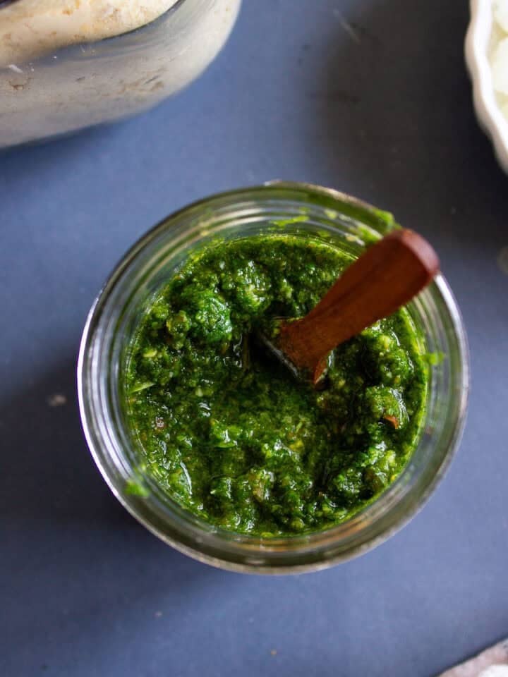 a jar of cilantro chutney top down with a spoon in it