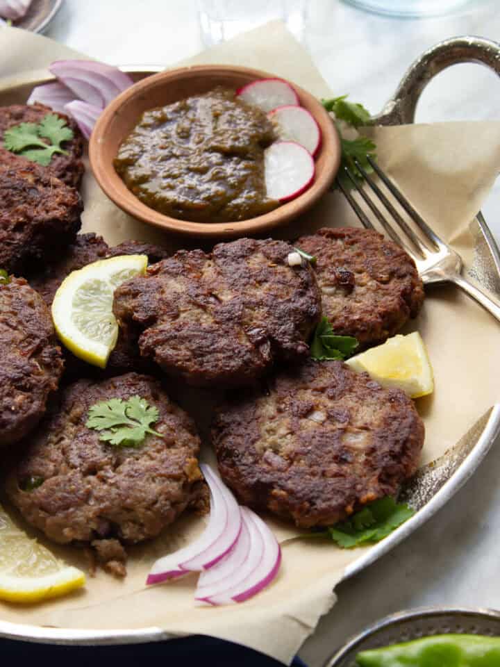 Kachay Qeemay Kay Kabab on a silver platter with parchment paper, chutney and garnishes