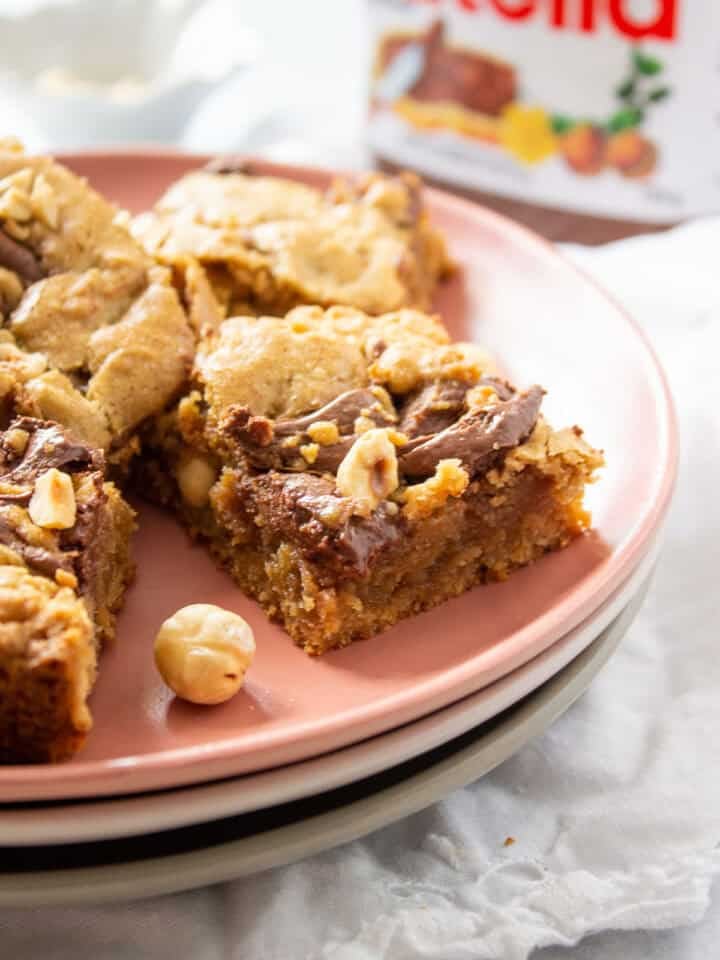 Nutella Blondies on a stack of 3 plates with a partial bottle of Nutella in the background