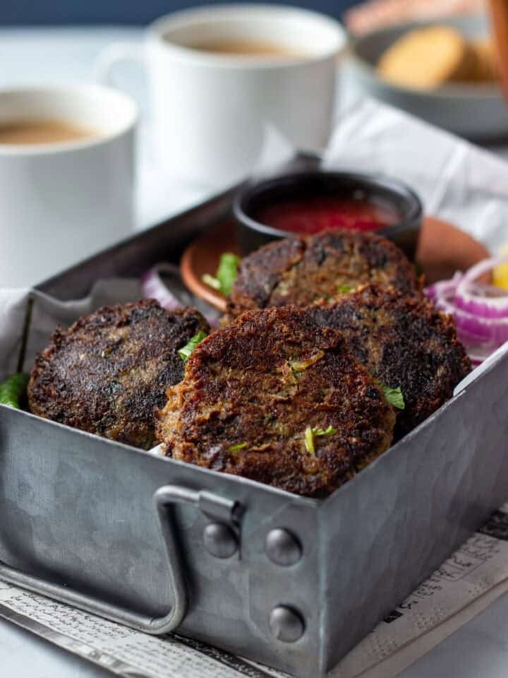 Shami Kabab in a metal tray garnished with cilantro and onions. two cups of chai.
