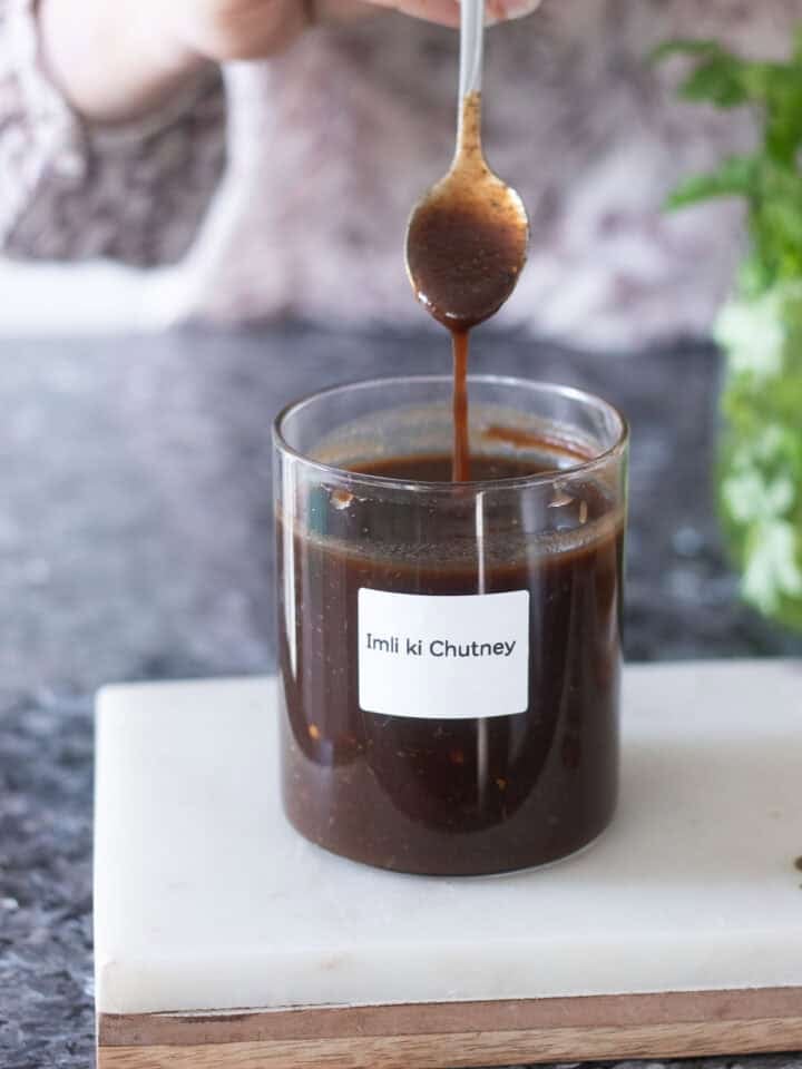imli chutney being dropped off from a spoon into a jar of chutney