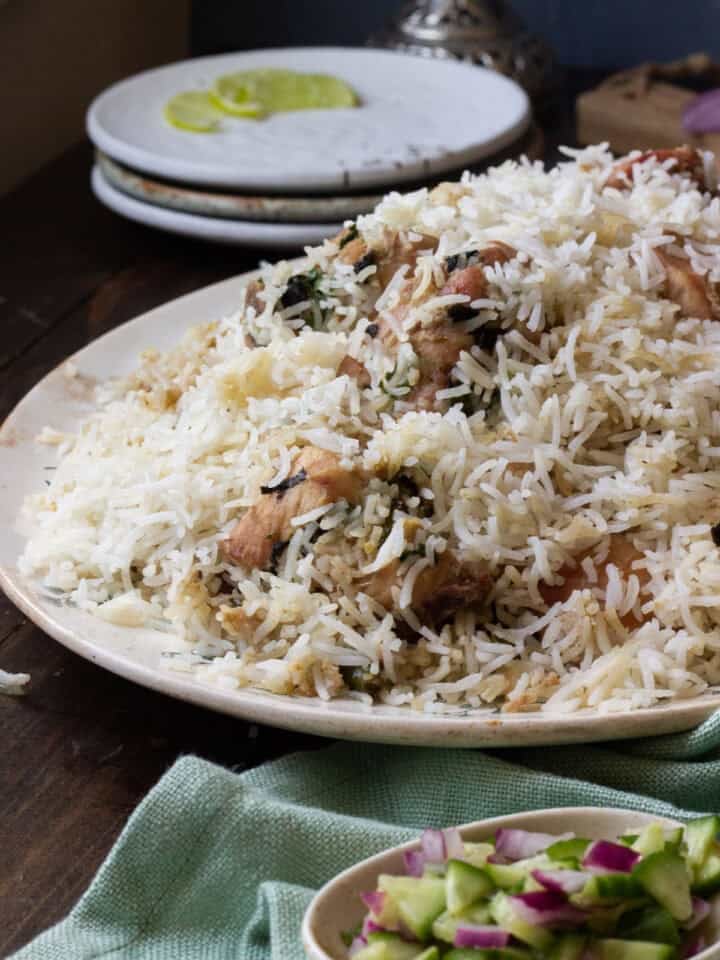 white biryani on a platter, a small plate with a chopped salad and a stack of plates