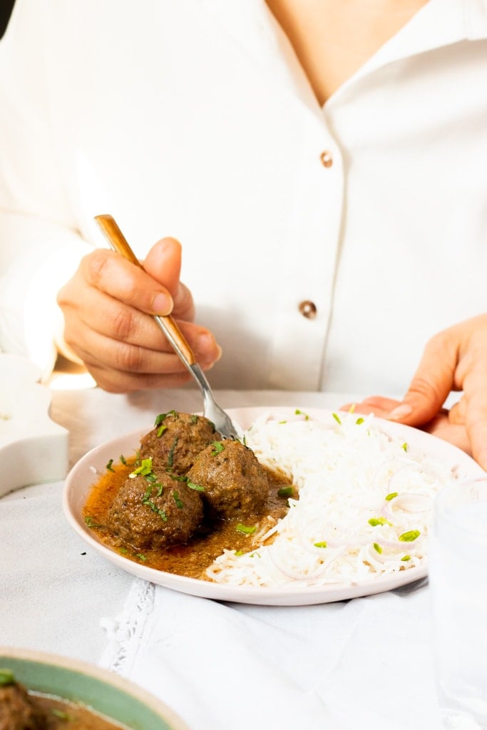 someone in a white shirt sitting at a table eating koftay ka salan and rice