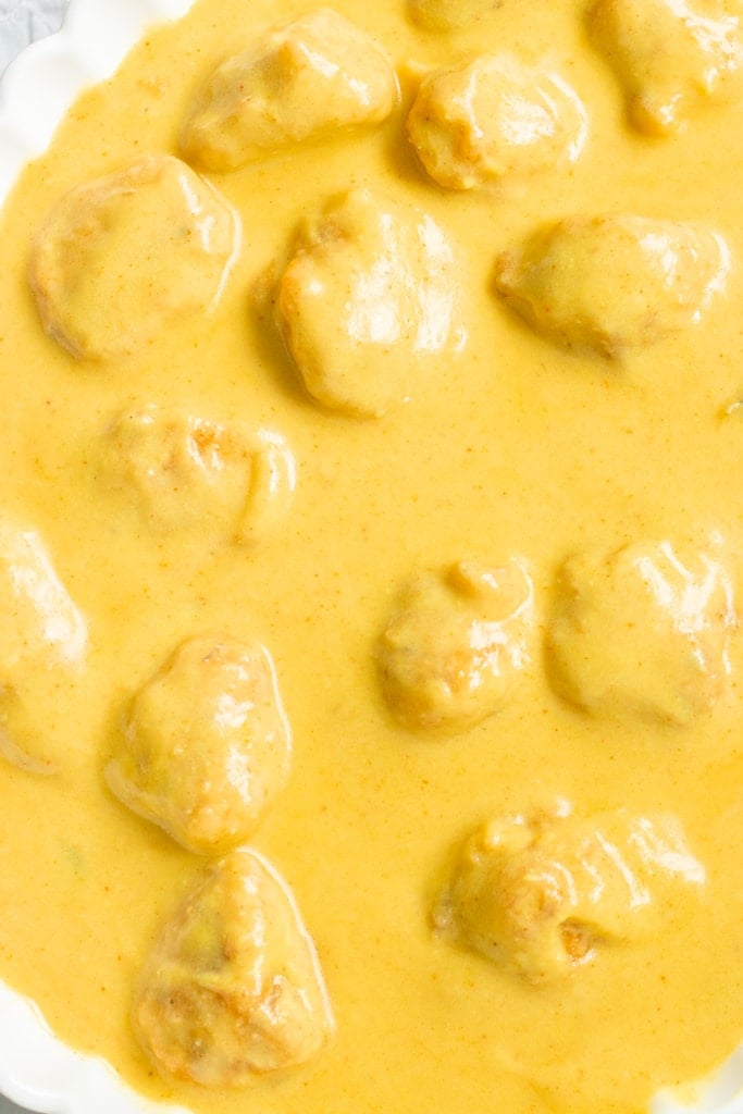 Creamy golden Karhi sauce with chunks of chicken in a white dish, viewed from above.