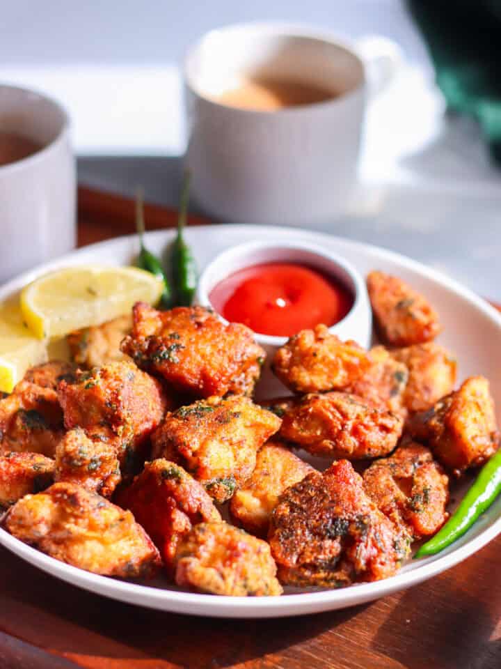 chicken pakoras on a plate with ketchup, lemon, green chilies